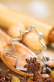 Christmas Baking. Tree shaped cookie cutter with star anise on wooden spoon surrounded by raisins, almonds and nuts, with a rolling pin in the back, sprinkled with powdered sugar (Selective Focus, Focus on the left side of the cookie cutter and on the upper part of the anise on the spoon)