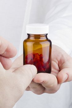 Close-up photograph of a hand holding a transparent glass container with red tablets.