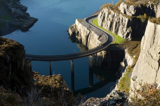 A road bridge on supports curves past cliffs over water.