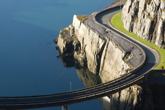 A road bridge on supports curves past cliffs over water.