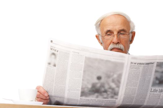 Portrait of an elder businessman reading a newspaper with a cup near him.