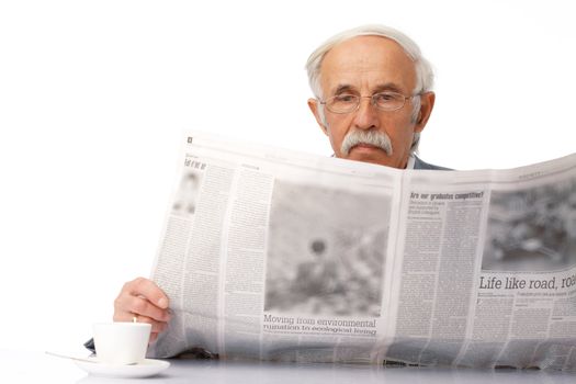 Portrait of an elder businessman reading a newspaper with a cup near him.