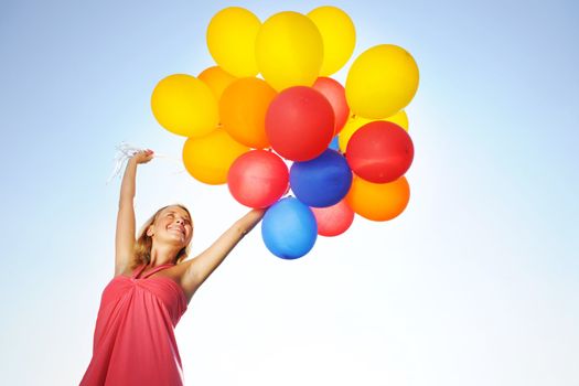 Woman holding balloons against sun and sky