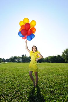 Woman holding balloons against sun and sky