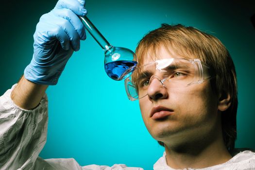 Scientist in protective wear and glasses looking at chemical flask