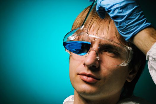 Scientist in protective wear and glasses looking at chemical flask