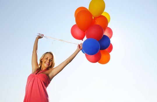 Woman holding balloons against sun and sky