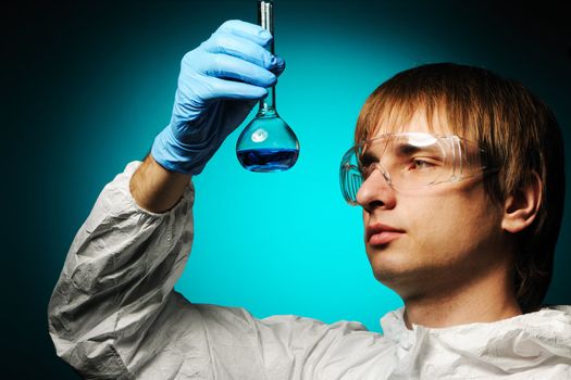 Scientist in protective wear and glasses looking at chemical flask
