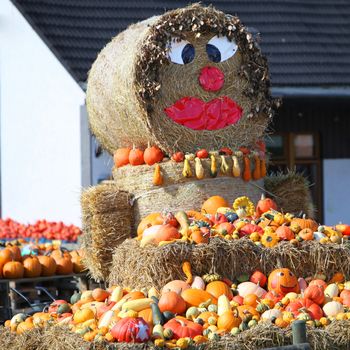 Fun autumn produce display on hay bales with a happy face painted on a circular bale topping pumpkins, squash and gourds on rectangular bales below 