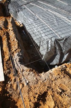 Excavations for the foundations of a new house with the main floor area covered in a sheet of plastic and a mesh of steel reinforcing rods 