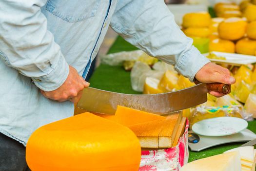 Male hands cutting dutch cheese at the market in Alkmaar