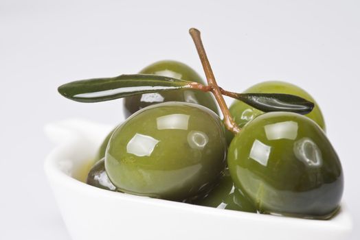 Green olives in a china spoon over a white background
