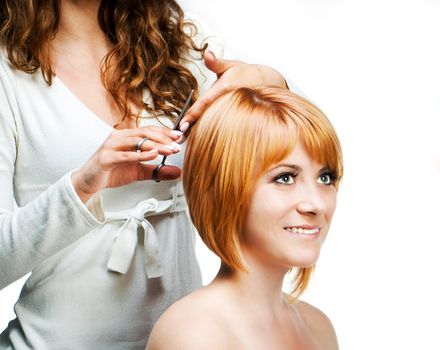 Young woman barber makes hairstyle for a girl isolated on white background