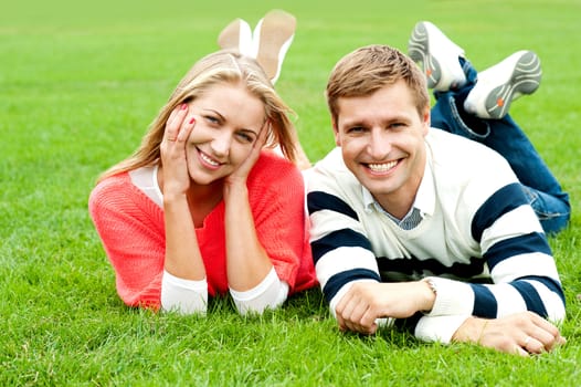 Happy young couple outdoors. Lying on lush green grass