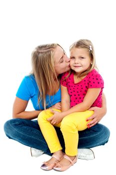 Beautiful mom with long hair sitting on floor with legs crossed and kissing her daughter