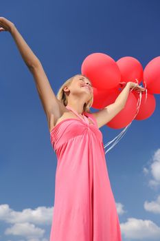 Woman holding balloons against sun and sky