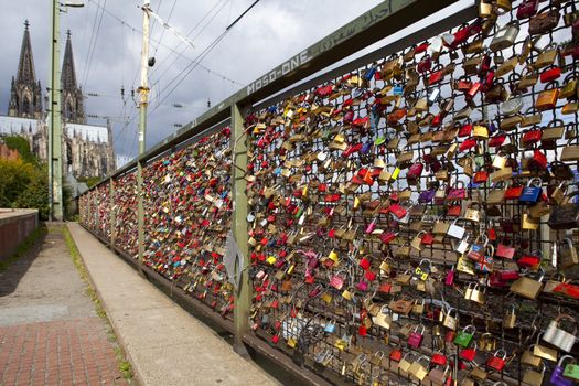 Locks on the Hohenzollern Bridge in Cologne.  Cologne Cathedral can be seen in the background.  Since 2008 people have placed love padlocks on the fence between the sidewalk and the tracks.