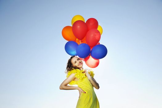 Woman holding balloons against sun and sky