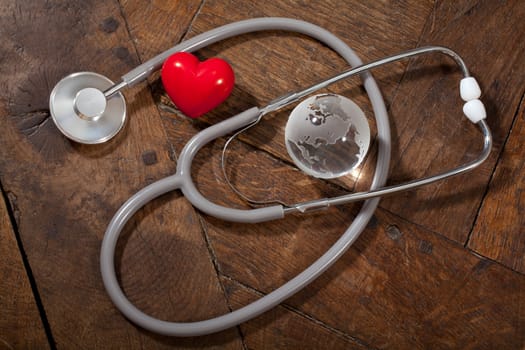 Stethoscope, heart and glass global earth on a wooden surface