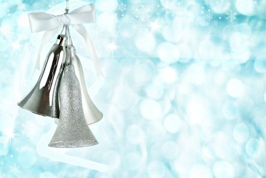 Silver bells hanging against an abstract background of icy blue holiday lights.
