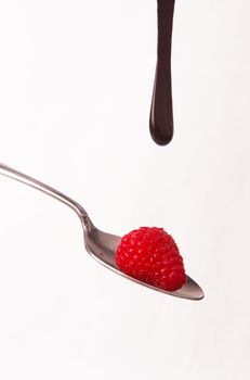 Raspberries on a spoon with chocolate syrup dropping on them