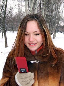 The girl in the winter in park with phone in a hand