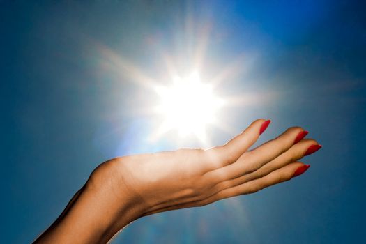 Woman hand holding the sun on a blue sky background