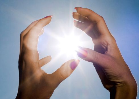 Woman hands touching the sun on a blue sky background