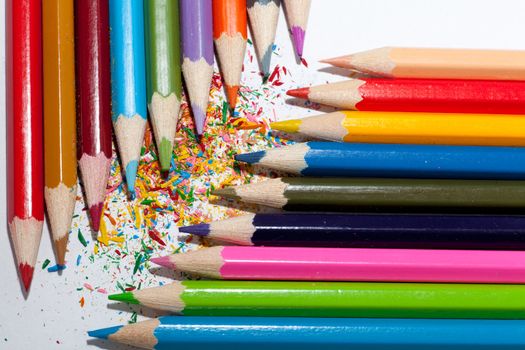 Colorful pencils (red, brown, blue, green, pink, orange, grey, violet ... ) positioned in two columns facing each other at 90 dergees angle forming a diagonal between their points against a white backgroung sprinkled with colorful shavings.