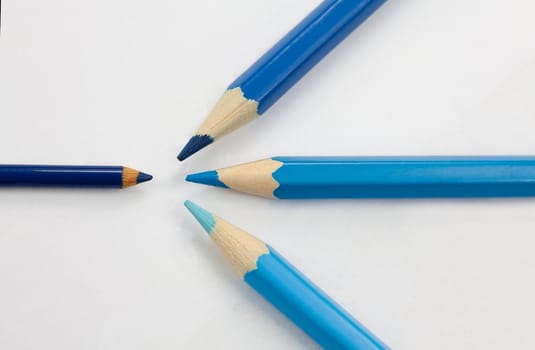 Big three blue color pencils of three different shades confronting one small dark blue color pencil against white background.