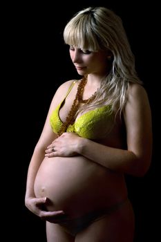 Young pregnant woman in yellow lingerie. Isolated on black