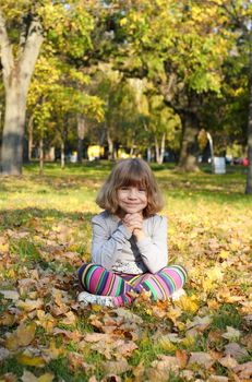 beautiful little girl sitting on autumn leaves in park