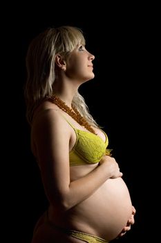 Happy pregnant young woman in yellow lingerie. Isolated on black