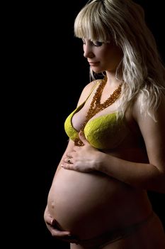 Pregnant young woman in yellow lingerie. Isolated on black