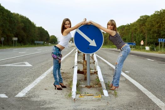 Two girls stand on a road near the sign
