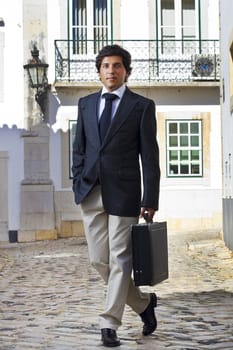 View of a happy business man with a black suitcase on a European city.