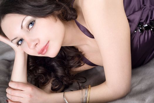 Beautiful young woman lying on grey fur coat