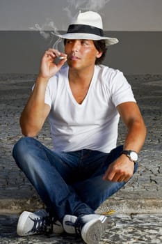 View of a handsome man with white shirt and hat on a urban city smoking a cigarette.