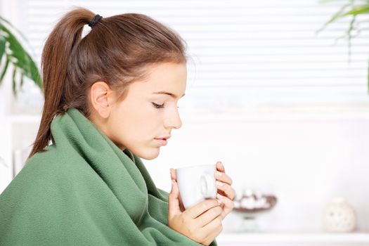 pretty young woman drinking tea  at home covered with blanket