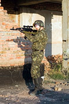 Soldier in camouflage ambushing behind brick wall