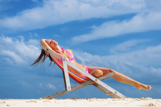 Girl on a tropical beach sitting in chaise lounge