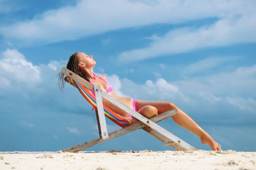 Girl on a tropical beach sitting in chaise lounge