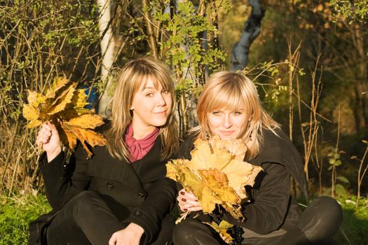 Two young women with autumn leaves in park