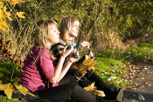 Two young women starts up soap bubble in park