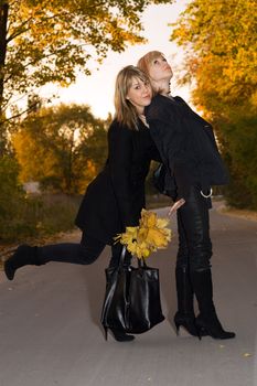 Two beauty young blondes with autumn leaves on a road