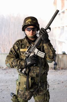 Handsome guy holding a rifle in front of abandoned house