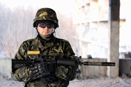 Handsome man with a rifle in front of neglected house