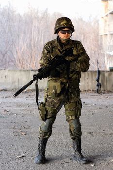 Military guy holding a gun in front of neglected building