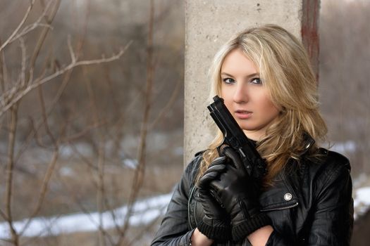 Scared young woman in leather jacket with a gun