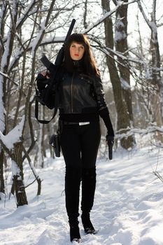 Beautiful young woman with a rifle and pistol in winter forest